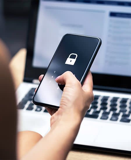 A person is holding a cell phone in front of a laptop.