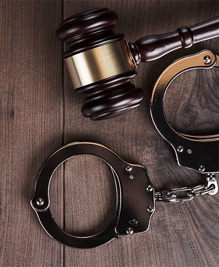 A pair of handcuffs and a judge 's gavel on a wooden table.