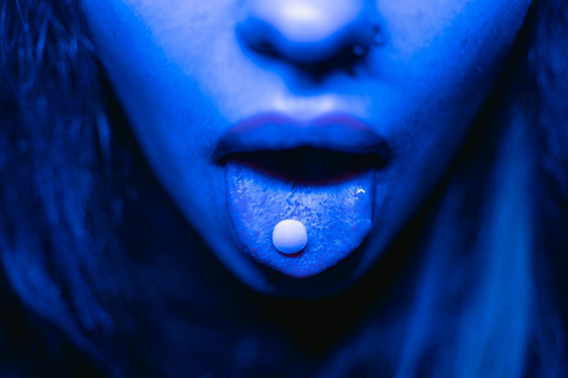 A close up of a woman 's face with a pill sticking out of her tongue.