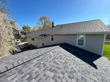 Rooftops and a gray-sided house with trees in the background on a sunny day