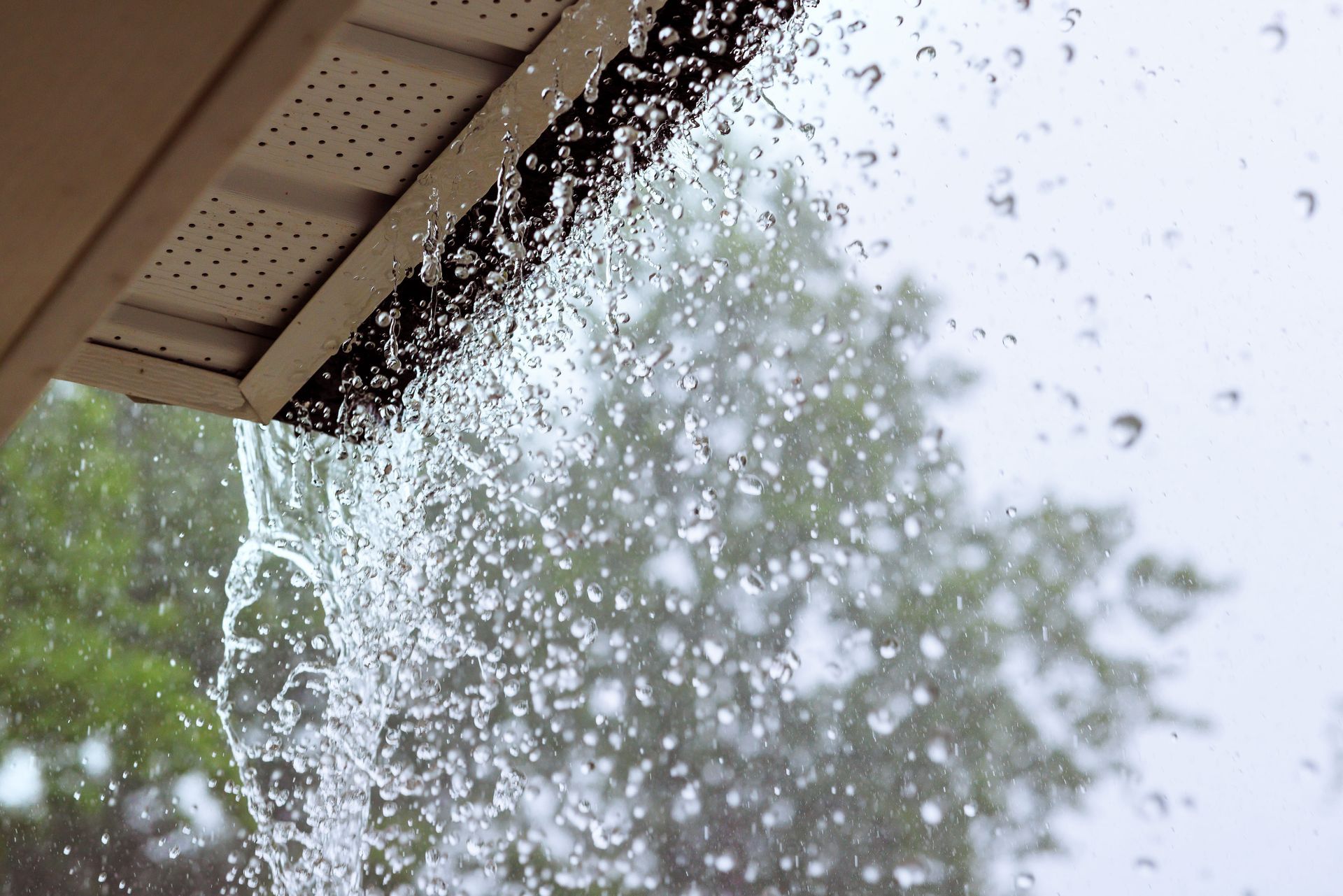 Water spraying from a roof gutter during rainfall, with trees in the background