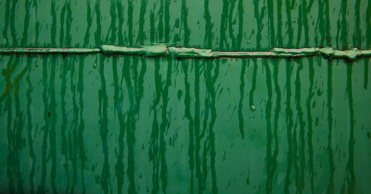 A closeup of green metal surface. Several wet drops and water paths lead down it from the top.