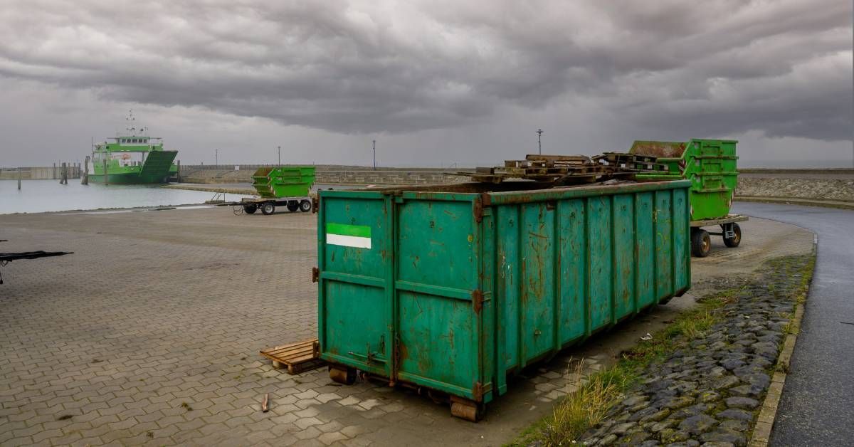 Open green dumpsters are available for use in wet area. Dark storm clouds fill the sky above.