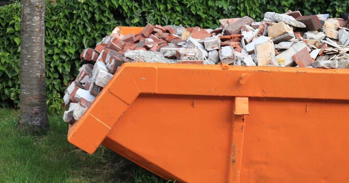 A small, orange dumpster unit on a grassy surface. It is filled to the very top with assorted bricks.