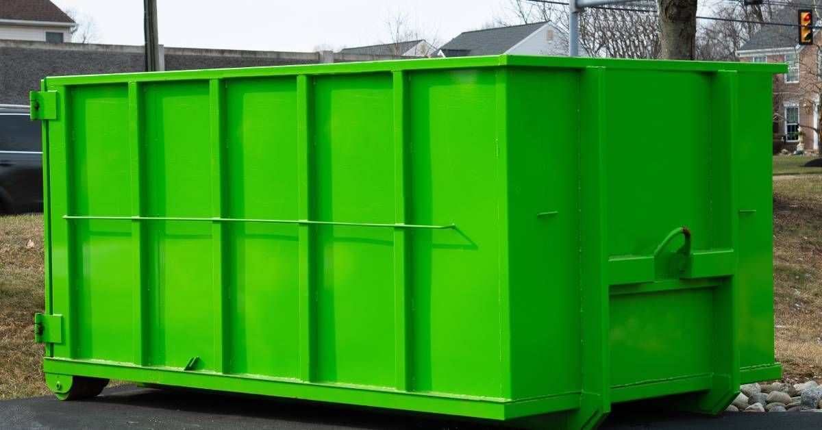 A large, bright green dumpster unit on an asphalt surface. The dumpster has a smooth surface without