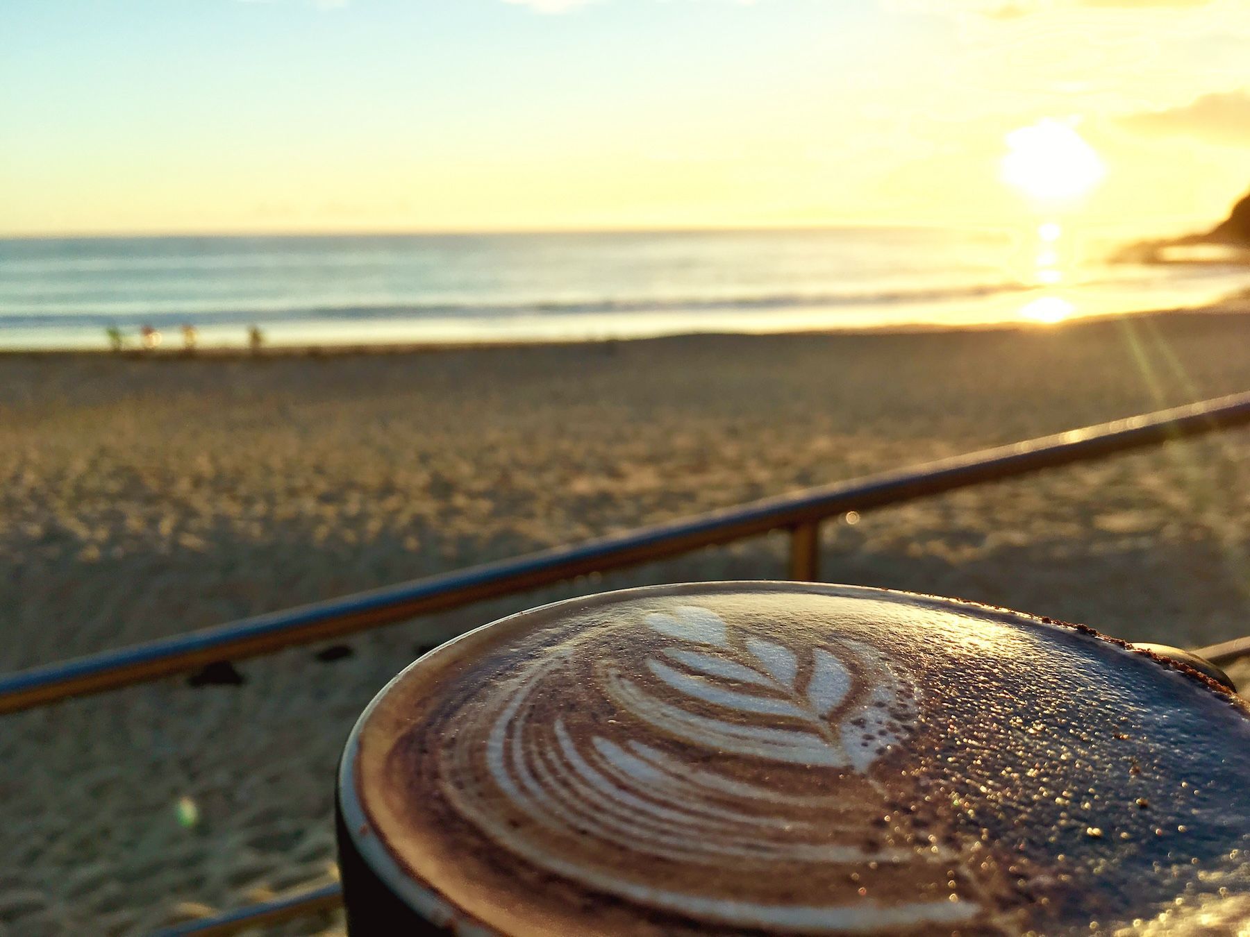 A cappuccino on a table in front of a view of Forster Main Beach at Sunrise
