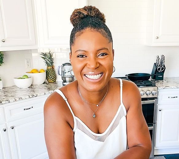 Woman smiling in a white kitchen, wearing a white top.