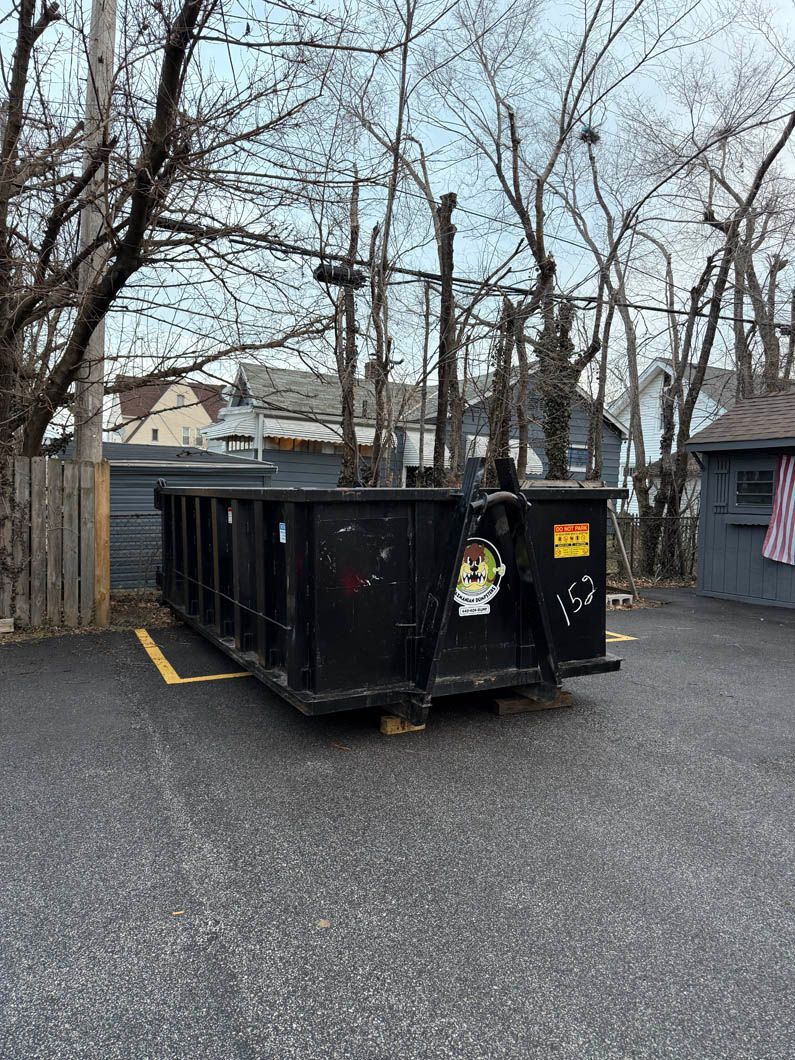 A dumpster is sitting in a parking lot next to a fence.