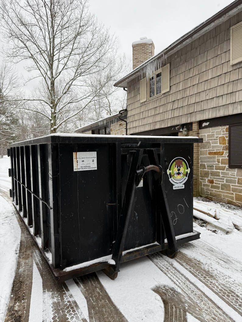 A dumpster is parked in front of a house in the snow.