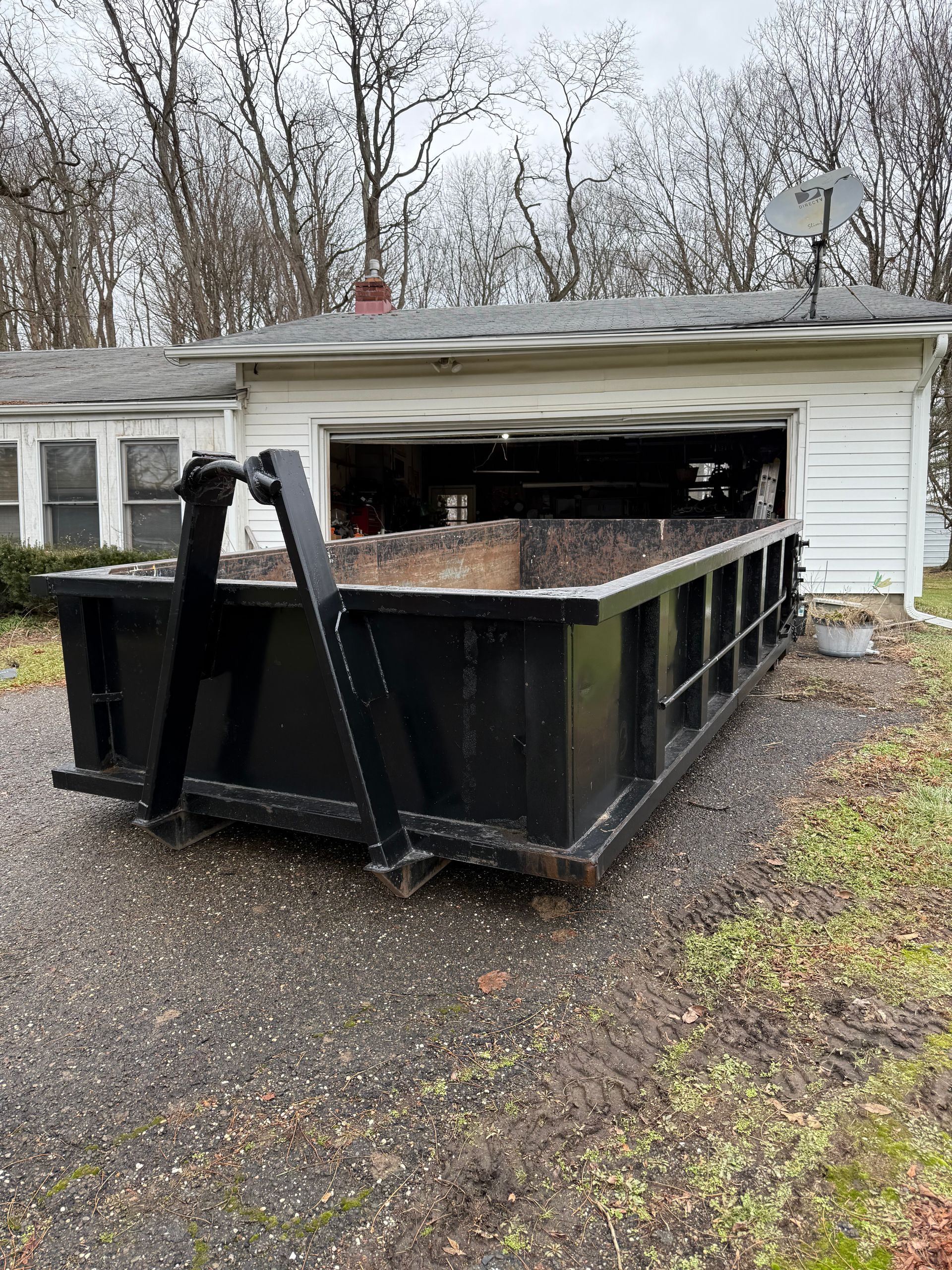 A dumpster is sitting in front of a house with a garage door open.