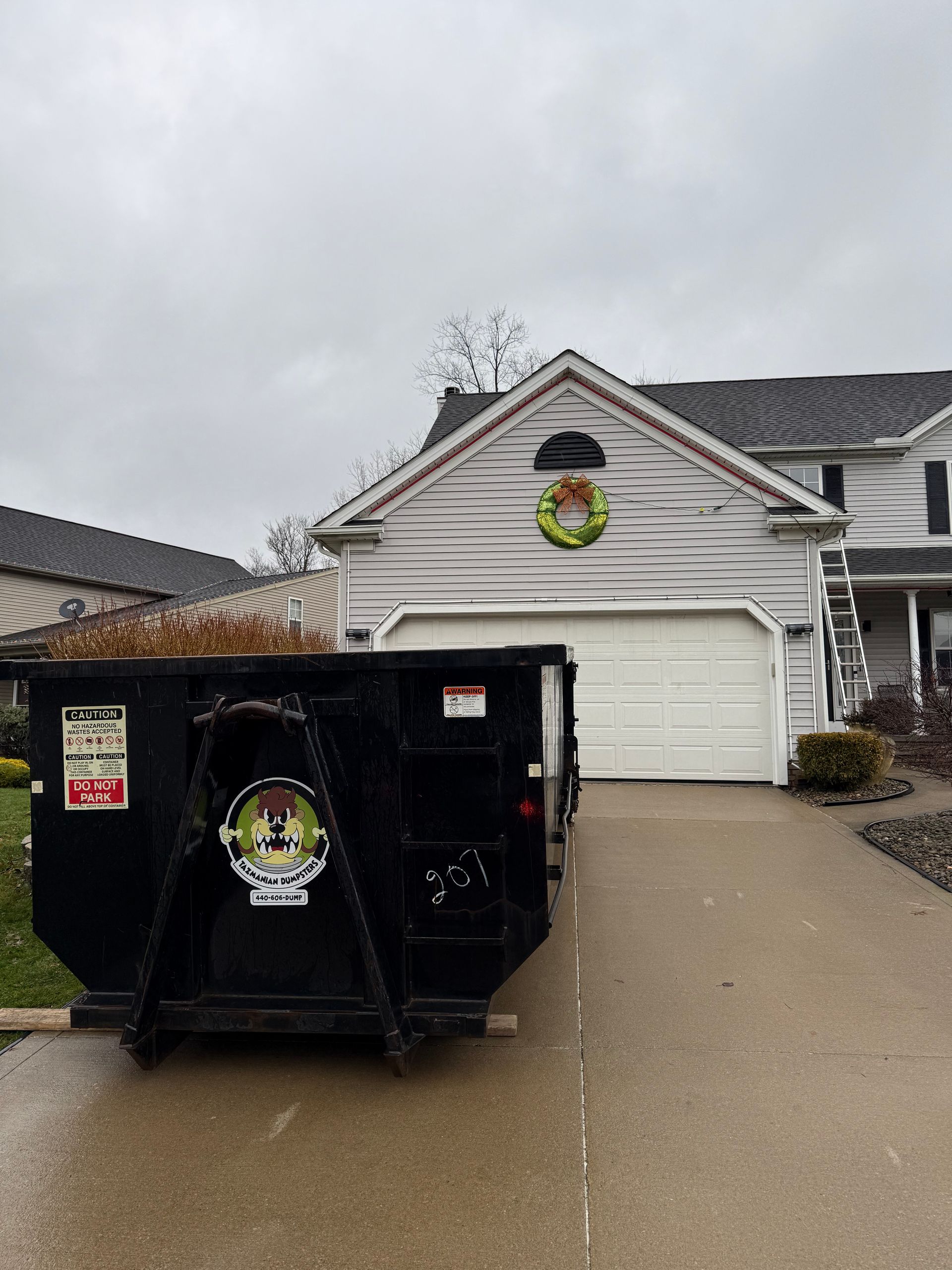A dumpster is parked in front of a house with a wreath on the roof.