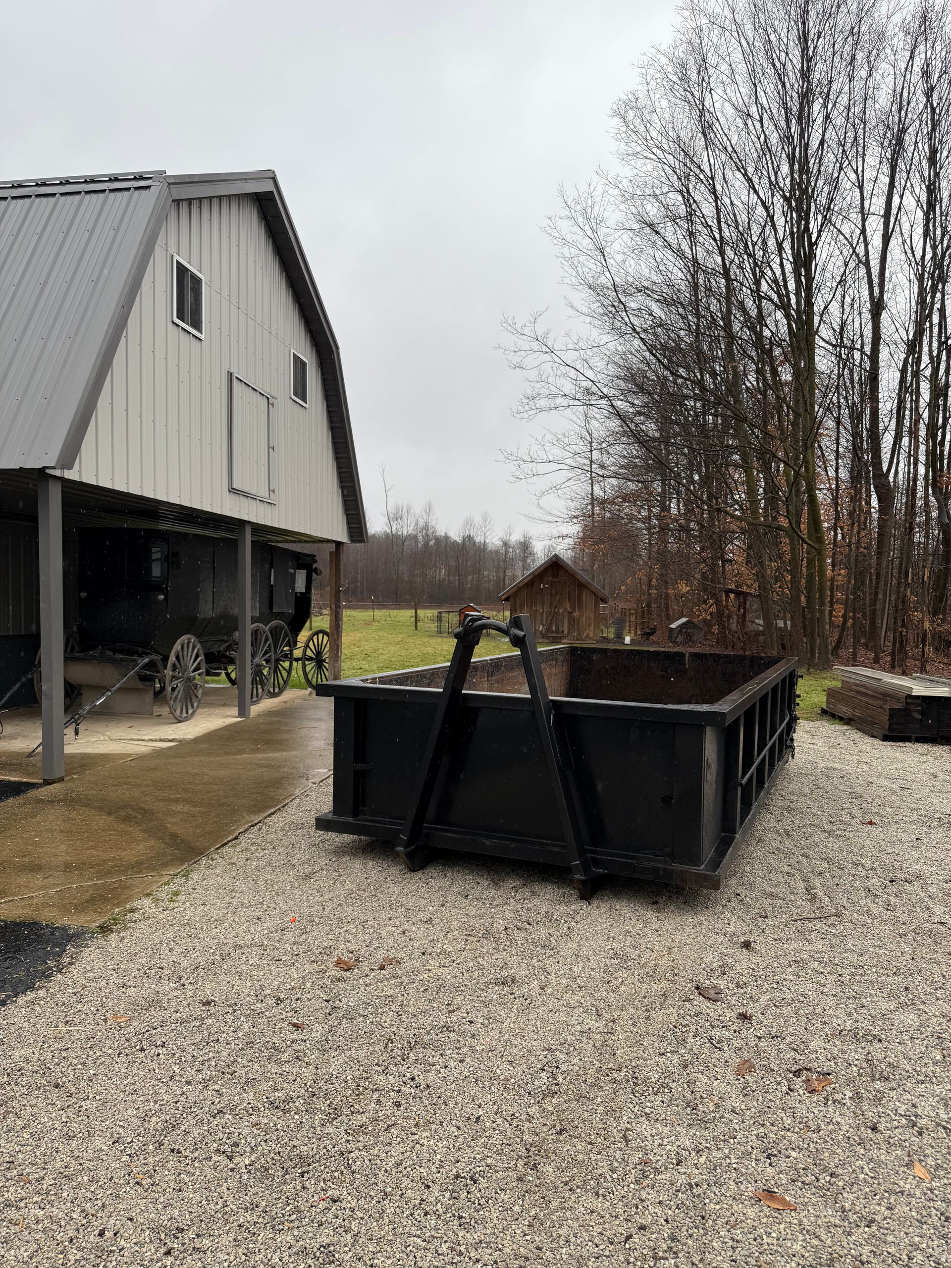 A large black dumpster is sitting in front of a barn.