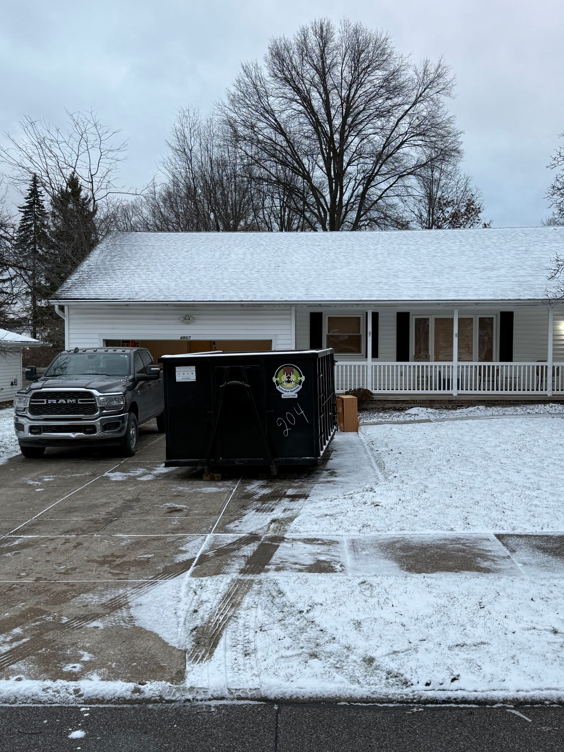 A black dumpster is parked in front of a house in the snow.