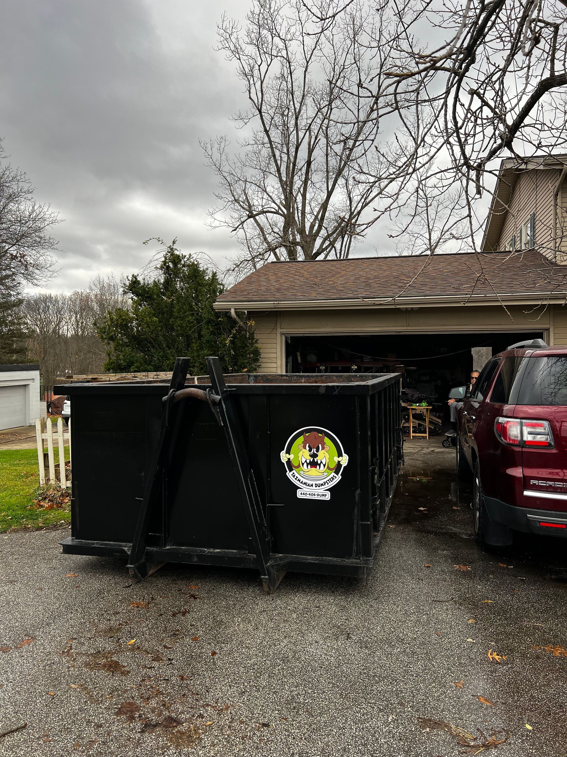 A dumpster is parked in a driveway in front of a house.