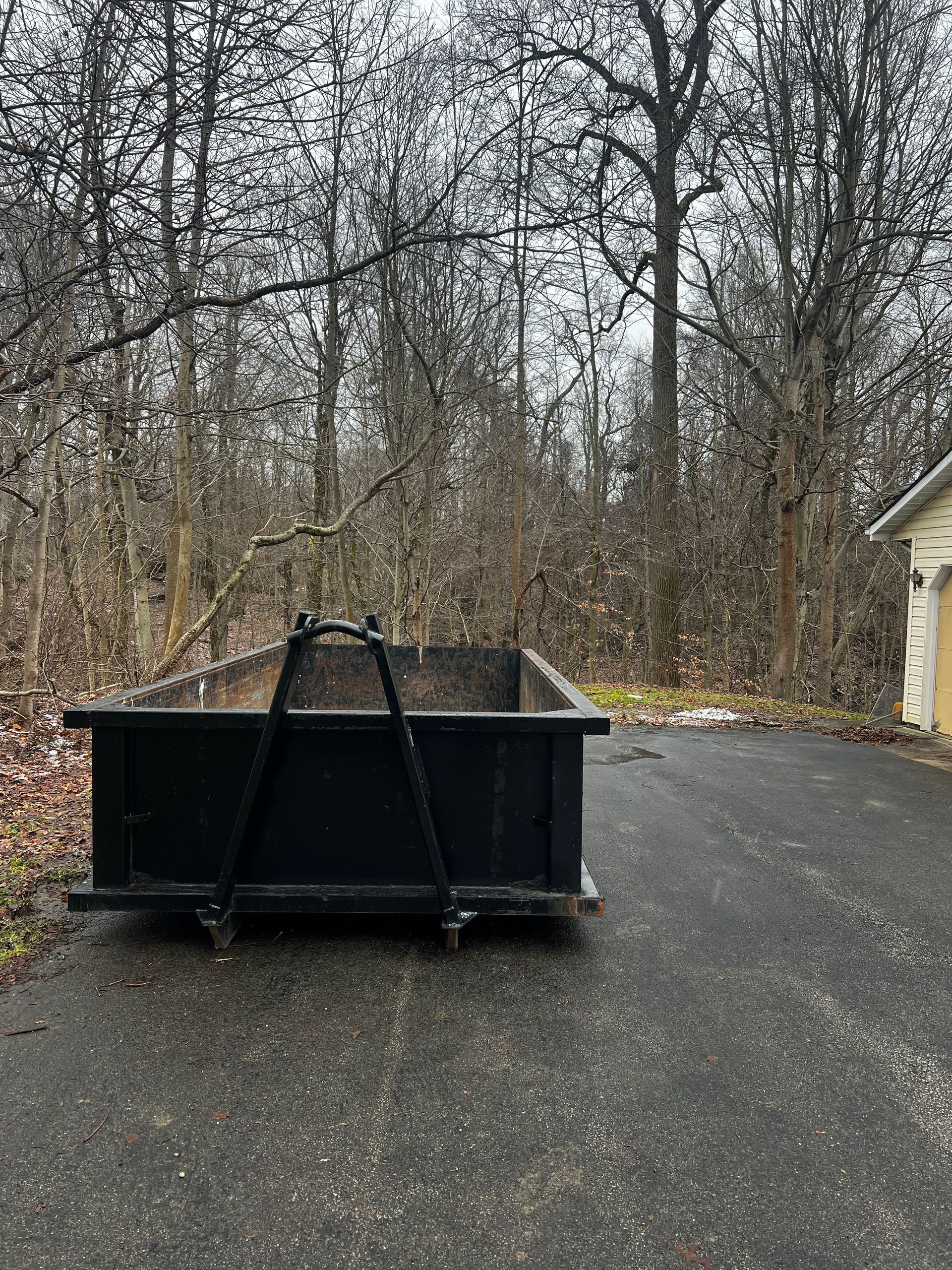 A dumpster is sitting on the side of a road next to a garage.
