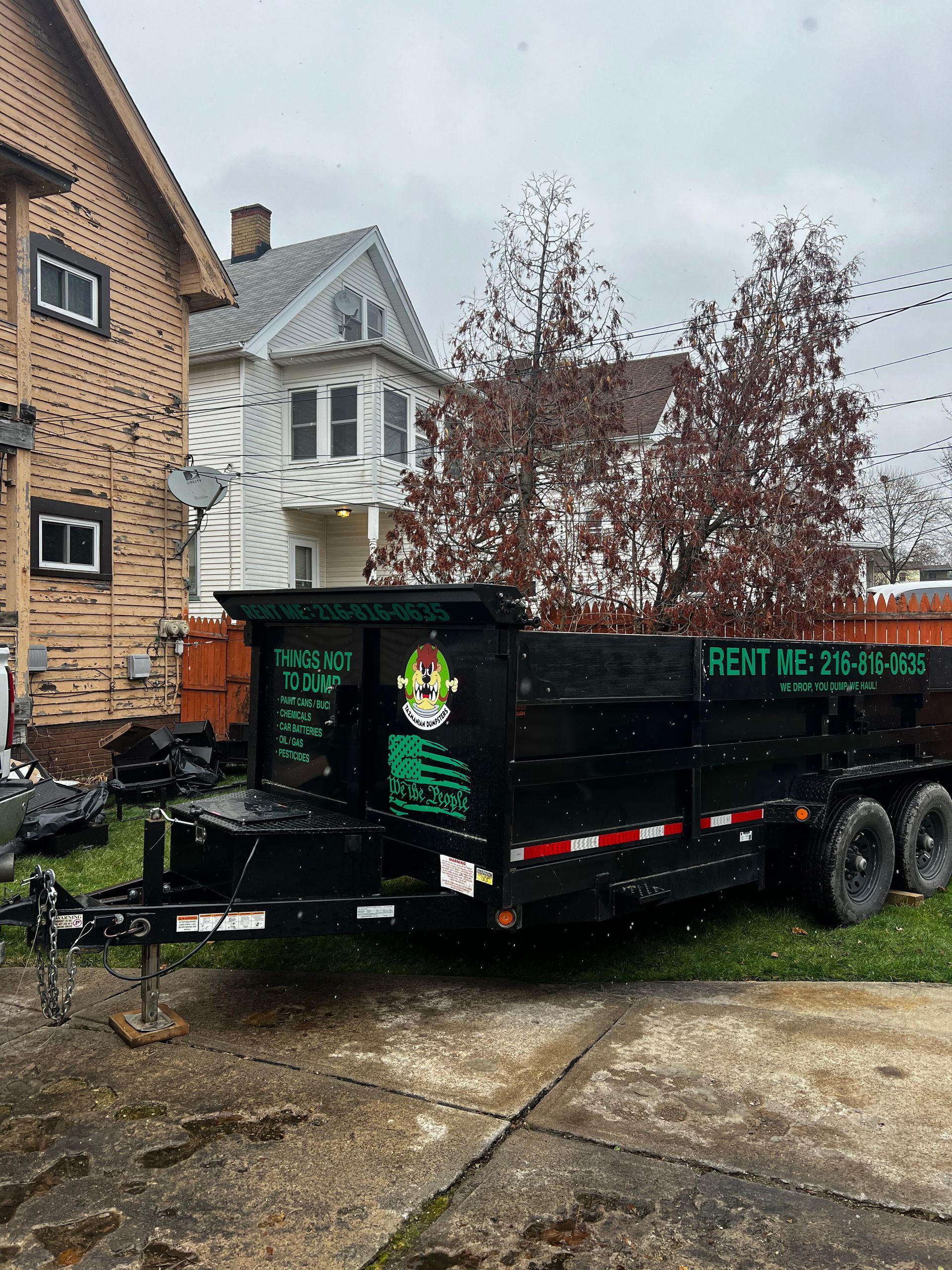 A dumpster trailer is parked in front of a brick house.