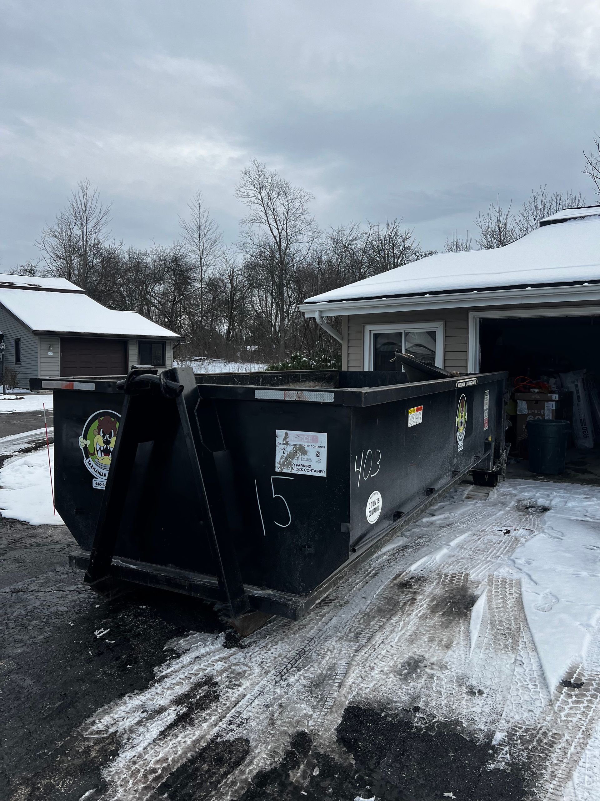 A dumpster is parked in front of a house in the snow.