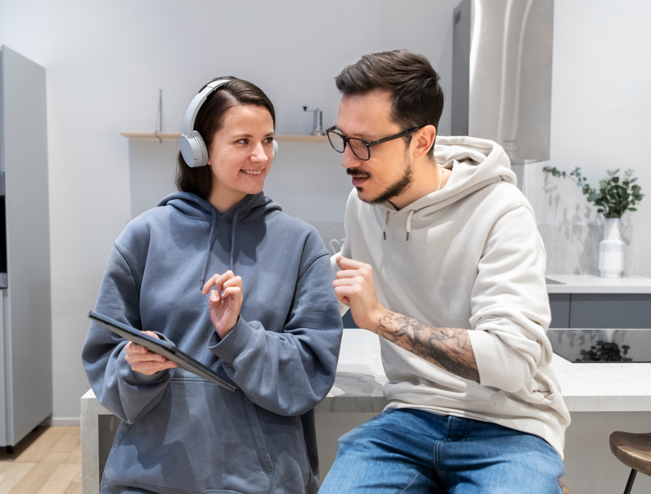 Mujer con auriculares y hombre mirando una tableta en una cocina, el hombre está gesticulando, ambos están sonriendo.