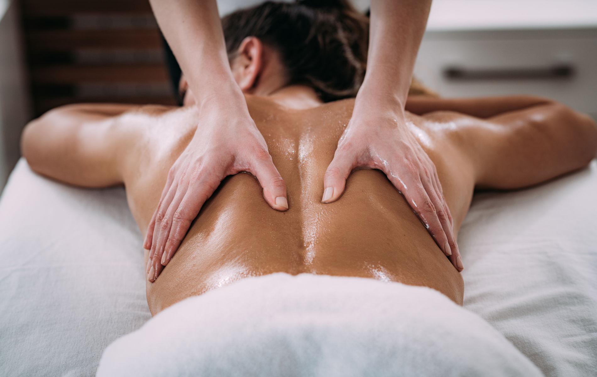 Hands massaging a person's back, on a massage table, in a well-lit room.