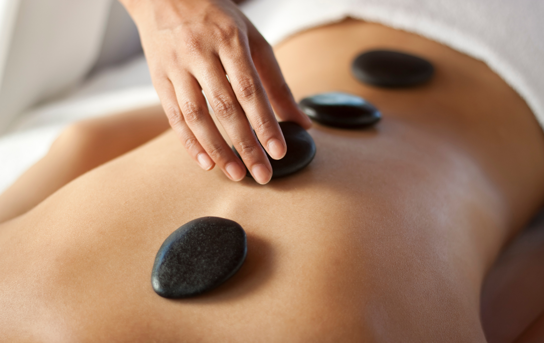 Person receiving hot stone massage on their back. A hand places a stone.