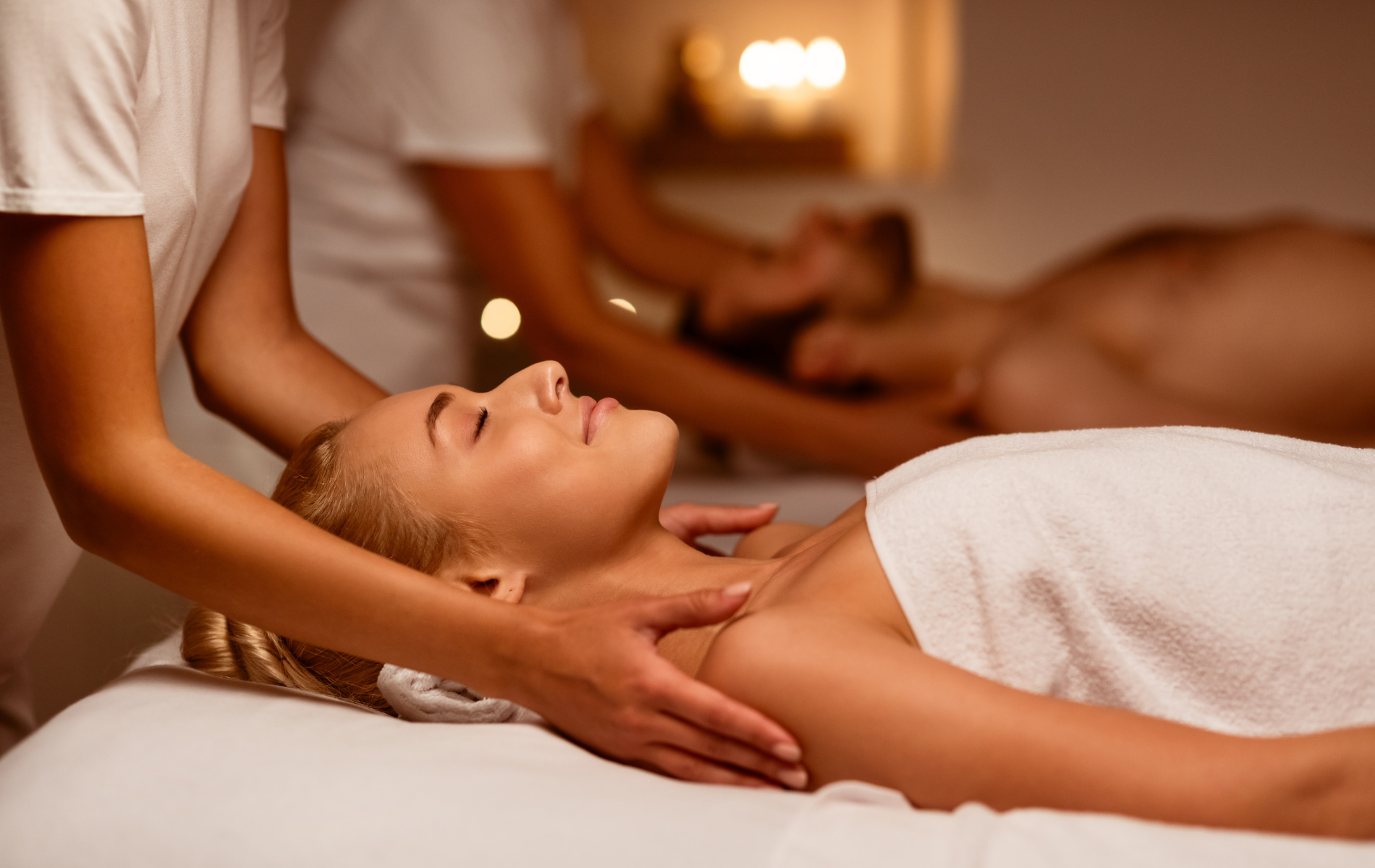 Woman receiving a shoulder massage at a spa; other person in the background also getting a massage.