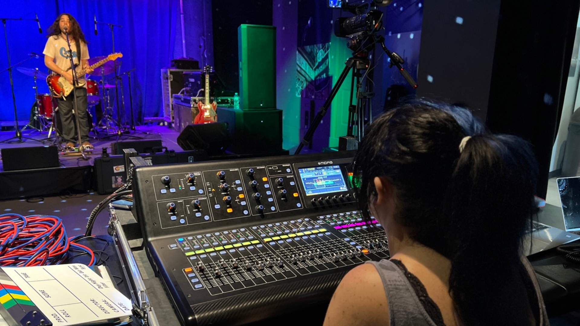 A person at a soundboard monitors a band performing on stage.