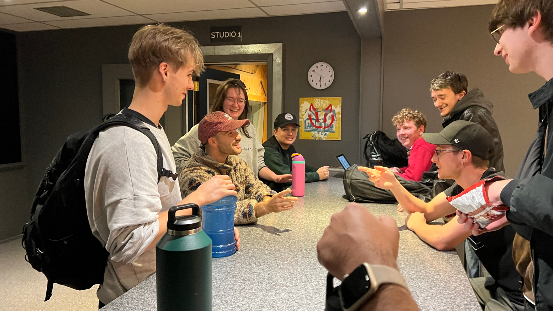 A group of OIART students standing around a high counter indoors, laughing and talking in a casual, brightly lit room.