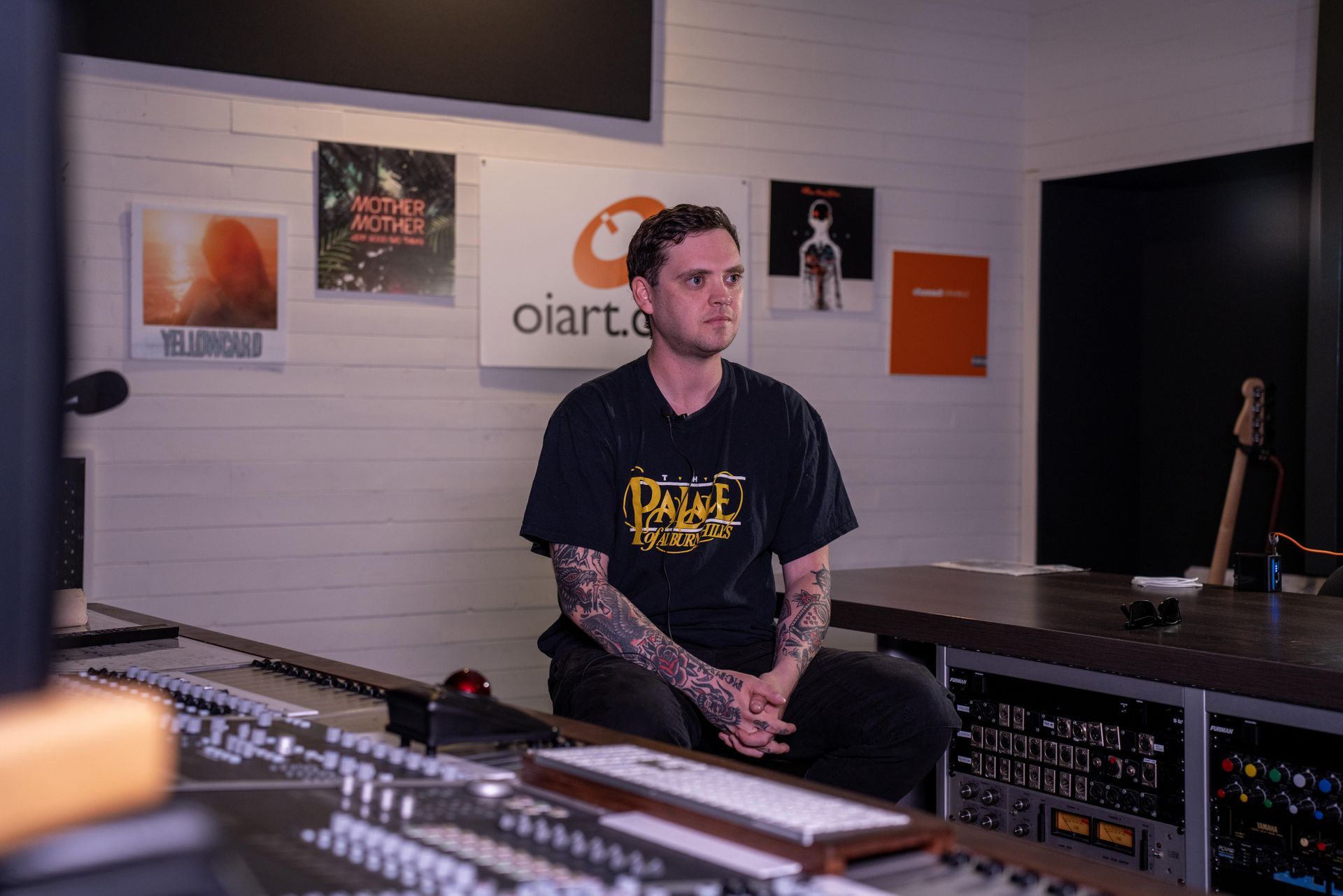 Matt sitting in a recording studio with audio equipment and wall posters behind him