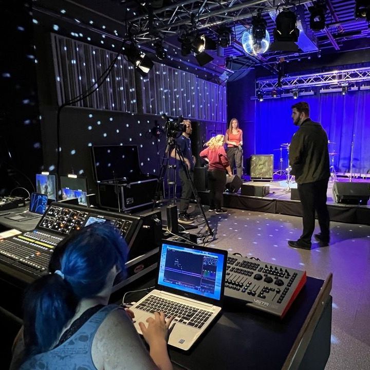 A woman with blue hair is using a laptop in front of a stage