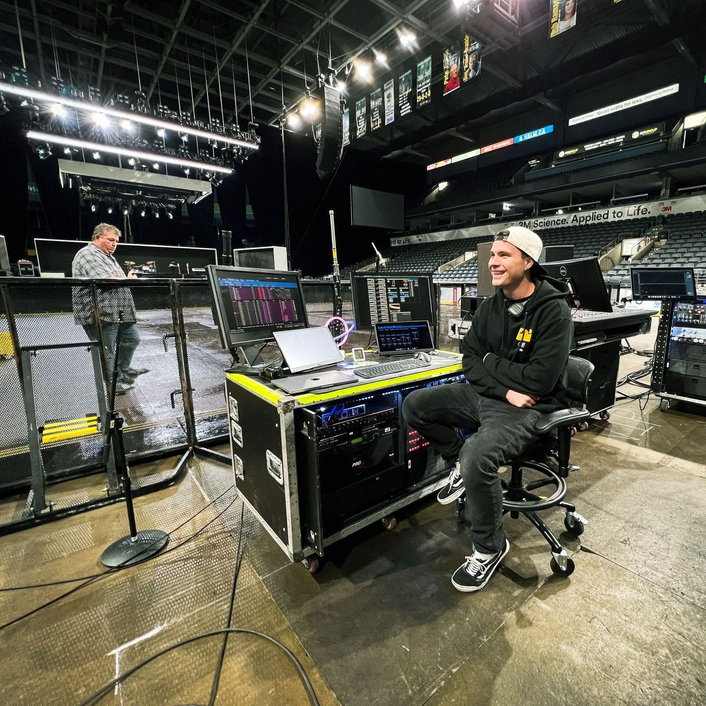 A man is sitting at a desk in a stadium with a laptop on it.