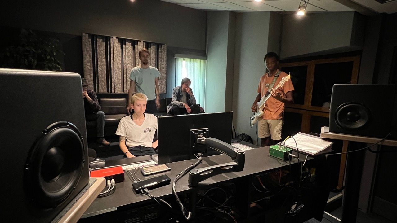A group of people are sitting at a table in a recording studio.