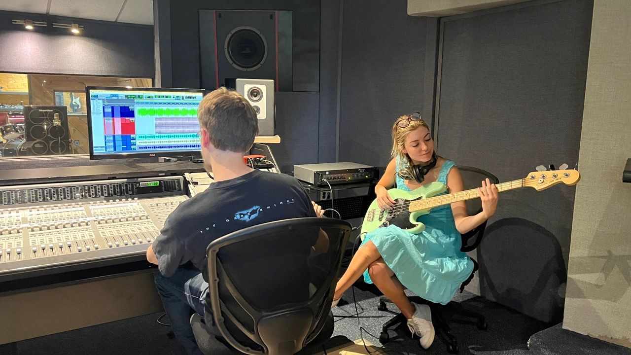 A man and a woman are playing guitars in a recording studio.