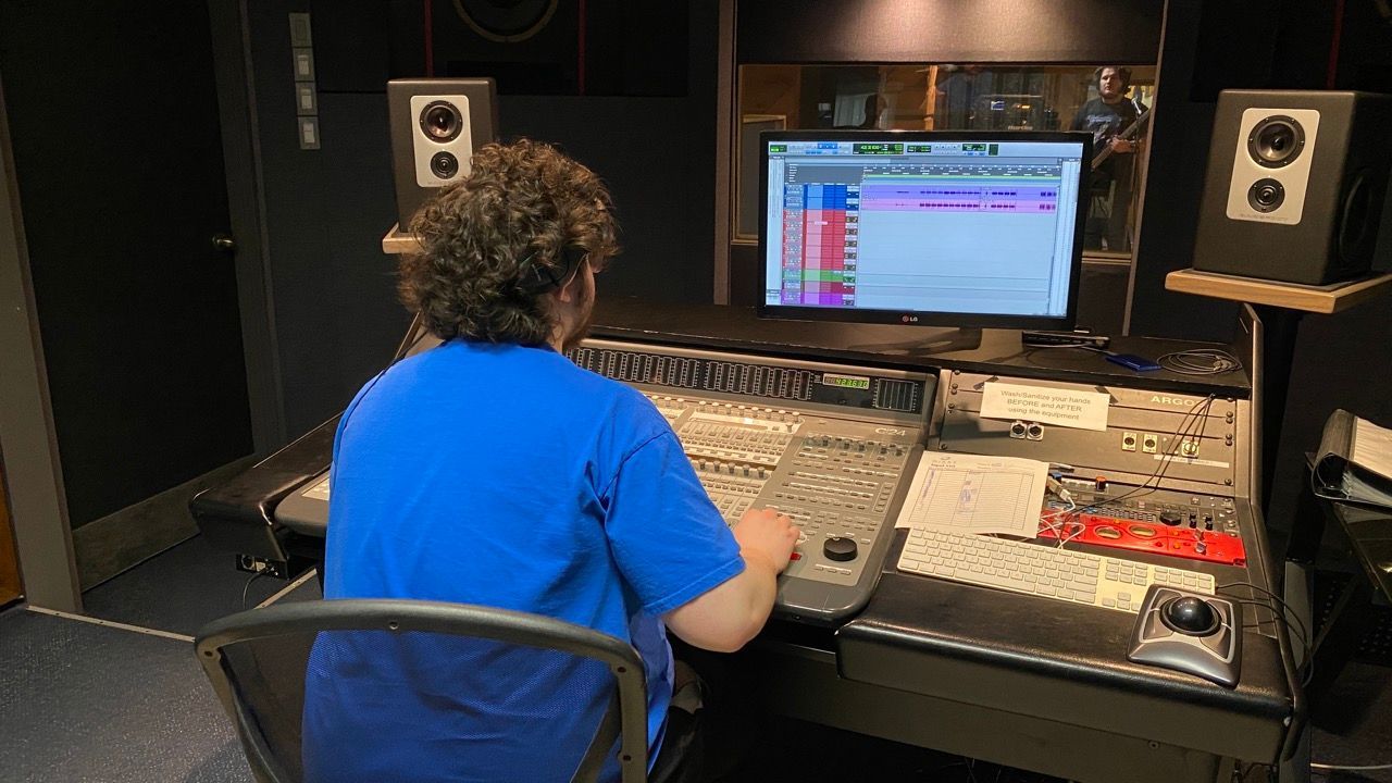 A man in a blue shirt is sitting at a desk in front of a computer.