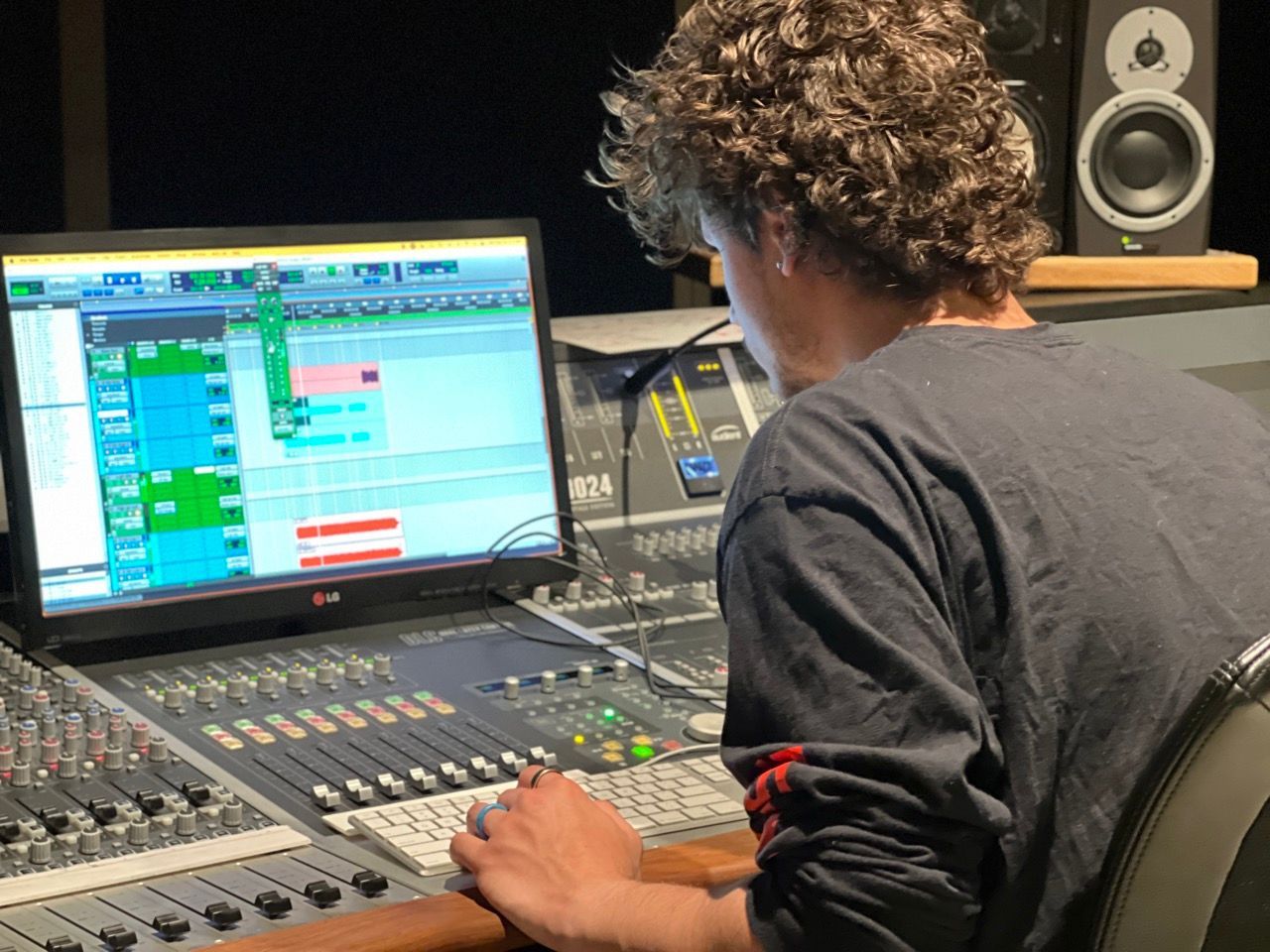 A man is sitting in front of a computer in a recording studio.