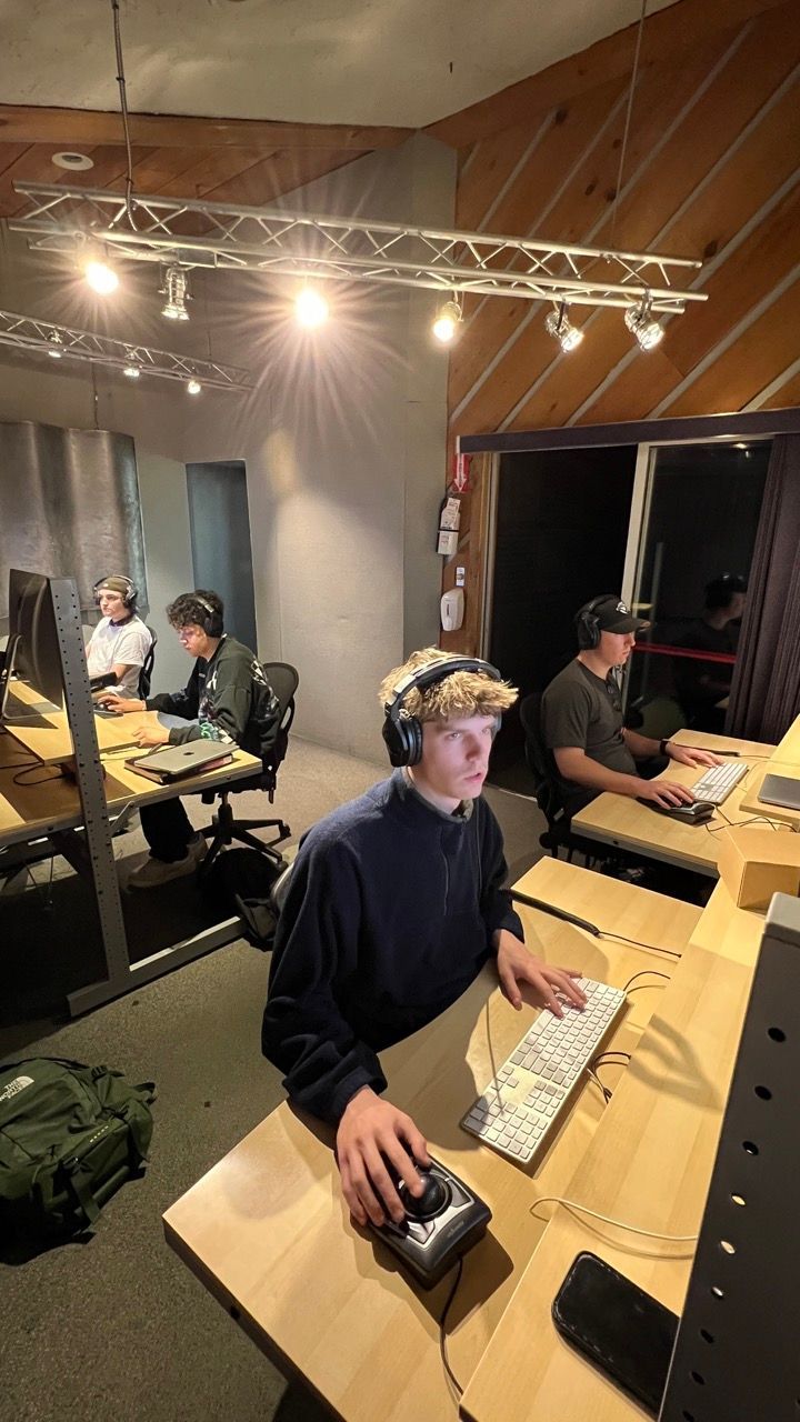 A man wearing headphones is sitting at a desk in front of a computer.