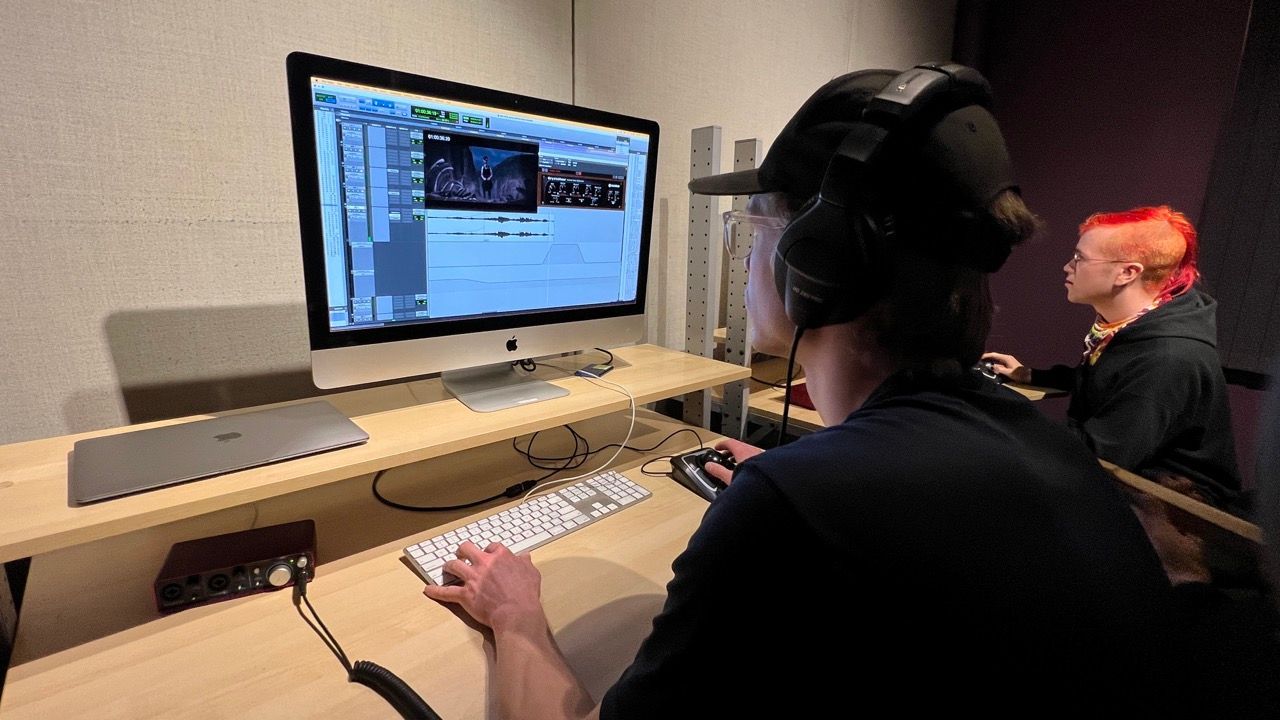 A woman wearing headphones is sitting at a desk in front of a computer monitor.