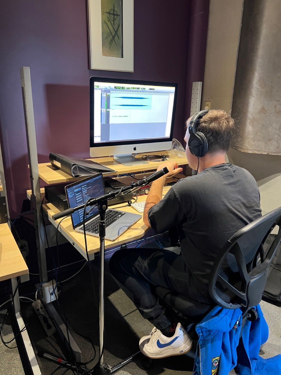A man wearing headphones is sitting at a desk in front of a computer.