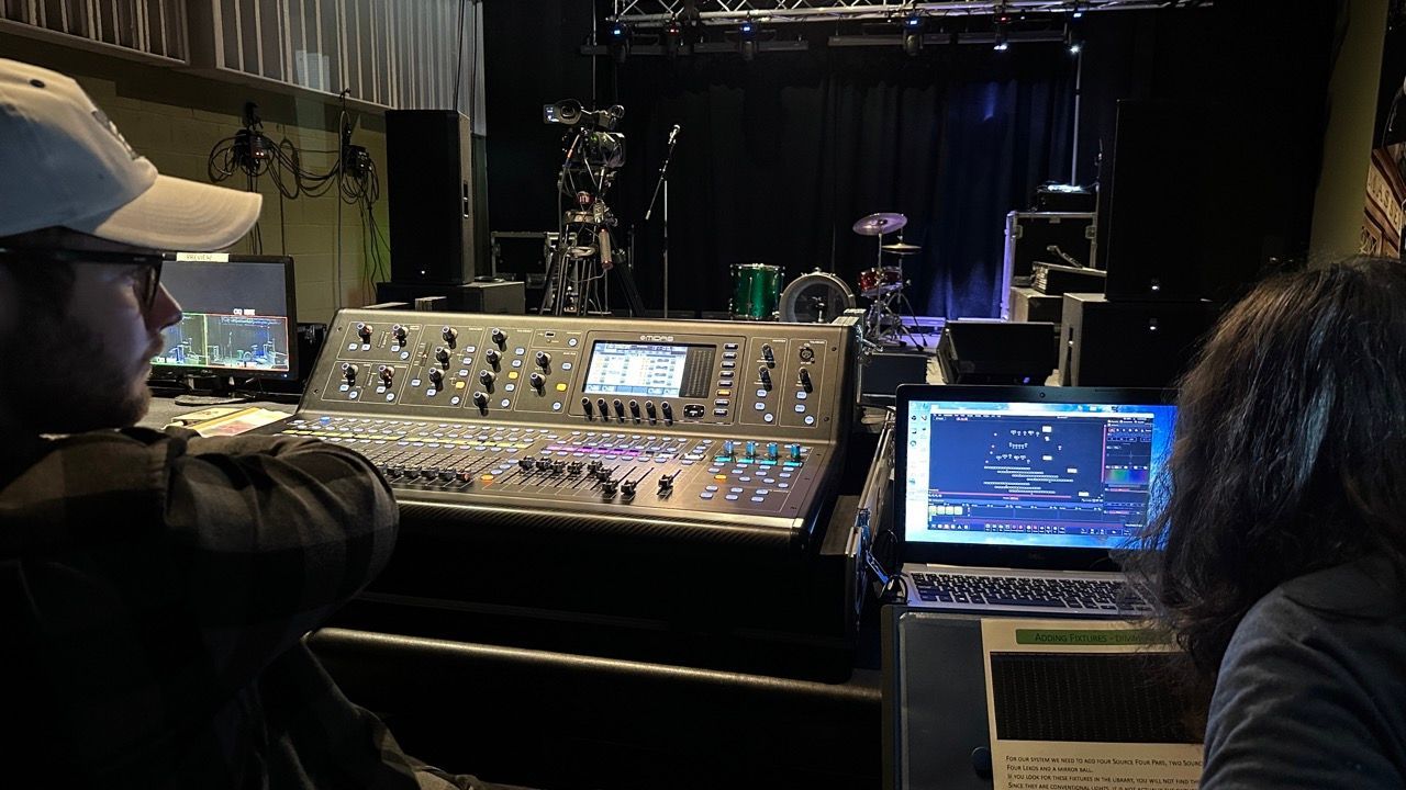 A man and woman are sitting in front of a mixer in a dark room.