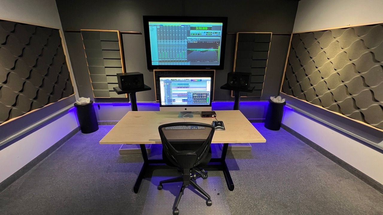 A recording studio with a desk , chair , monitors and a projector screen.