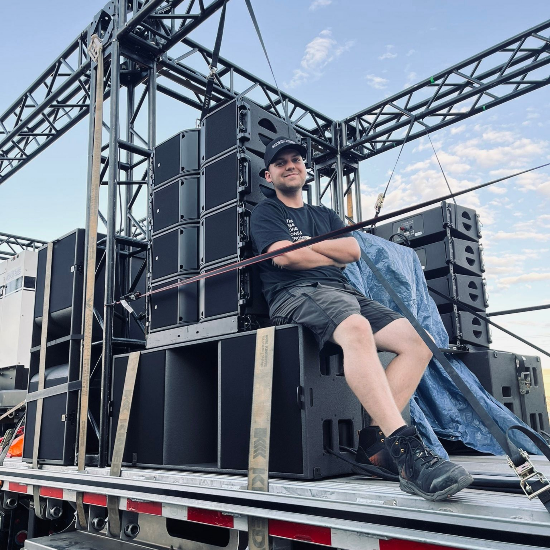 Avery Szumlamski sitting on stacked black speakers on a flatbed truck at an outdoor event stage