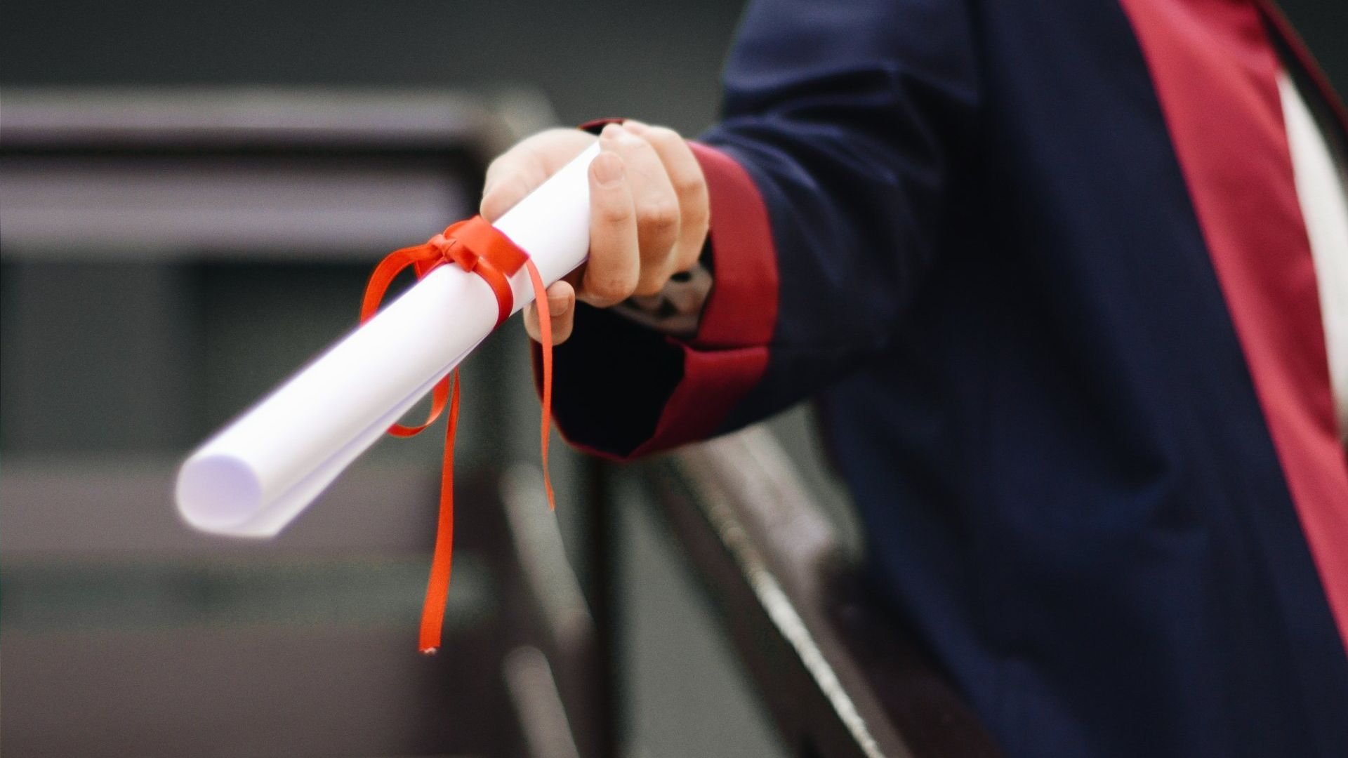 A person is holding a diploma with a red ribbon around it.