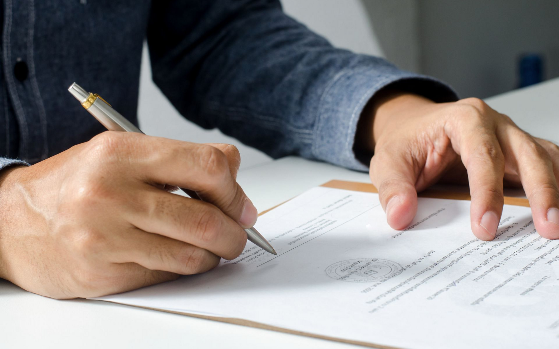 Person's hands writing with a pen on paper, on a clipboard.