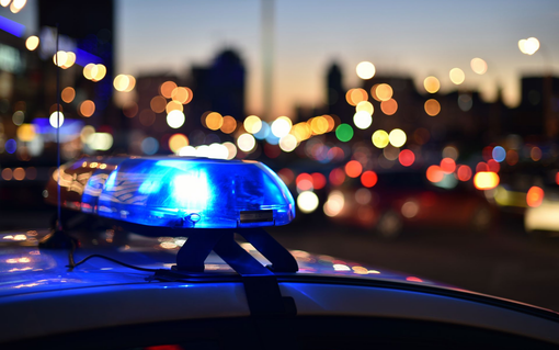 Blue police car lights flashing at dusk with city lights in background.