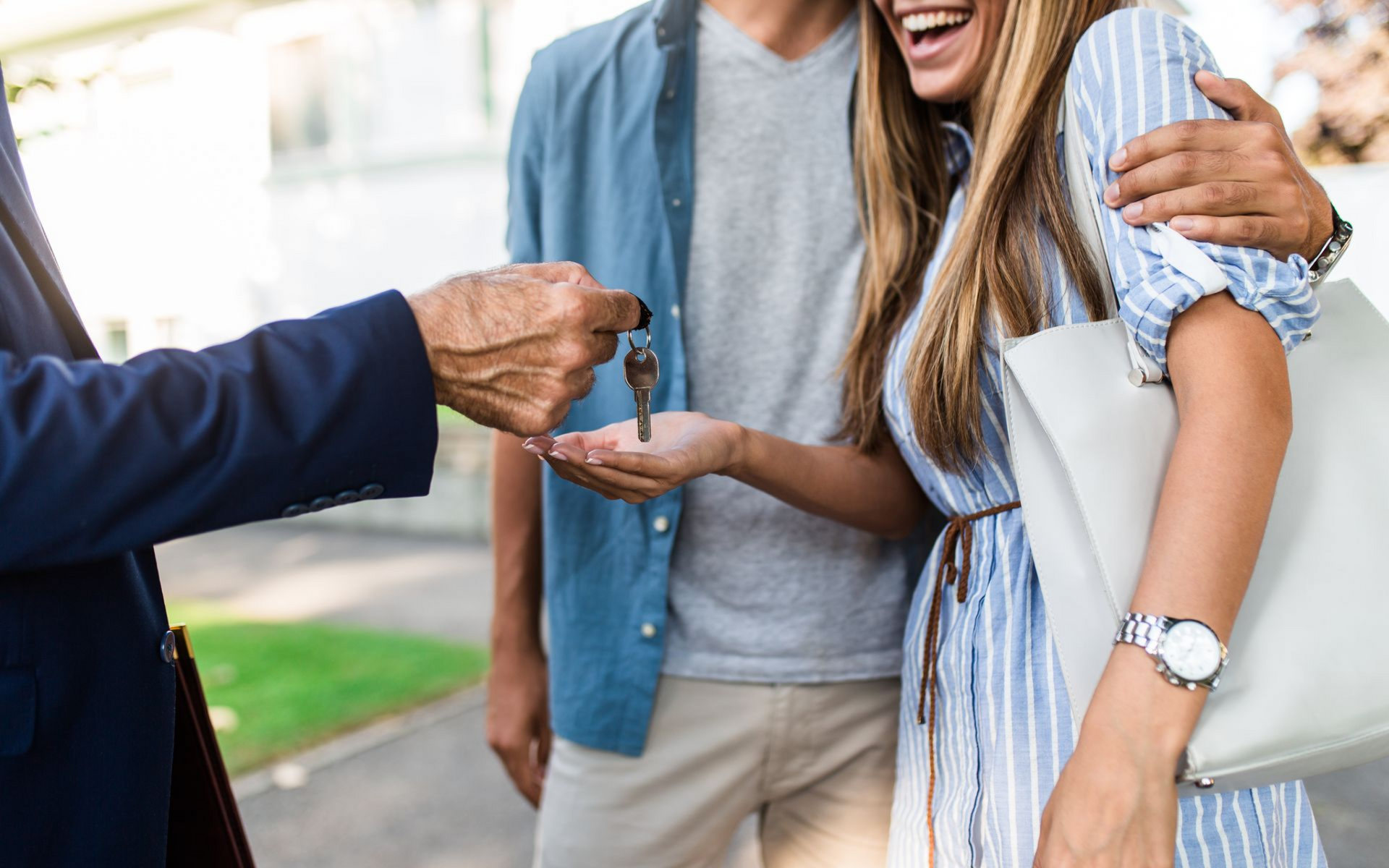 Real estate agent handing keys to a smiling couple, outdoors.