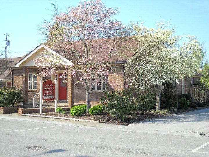 Brick building with red door and sign, surrounded by blooming trees.