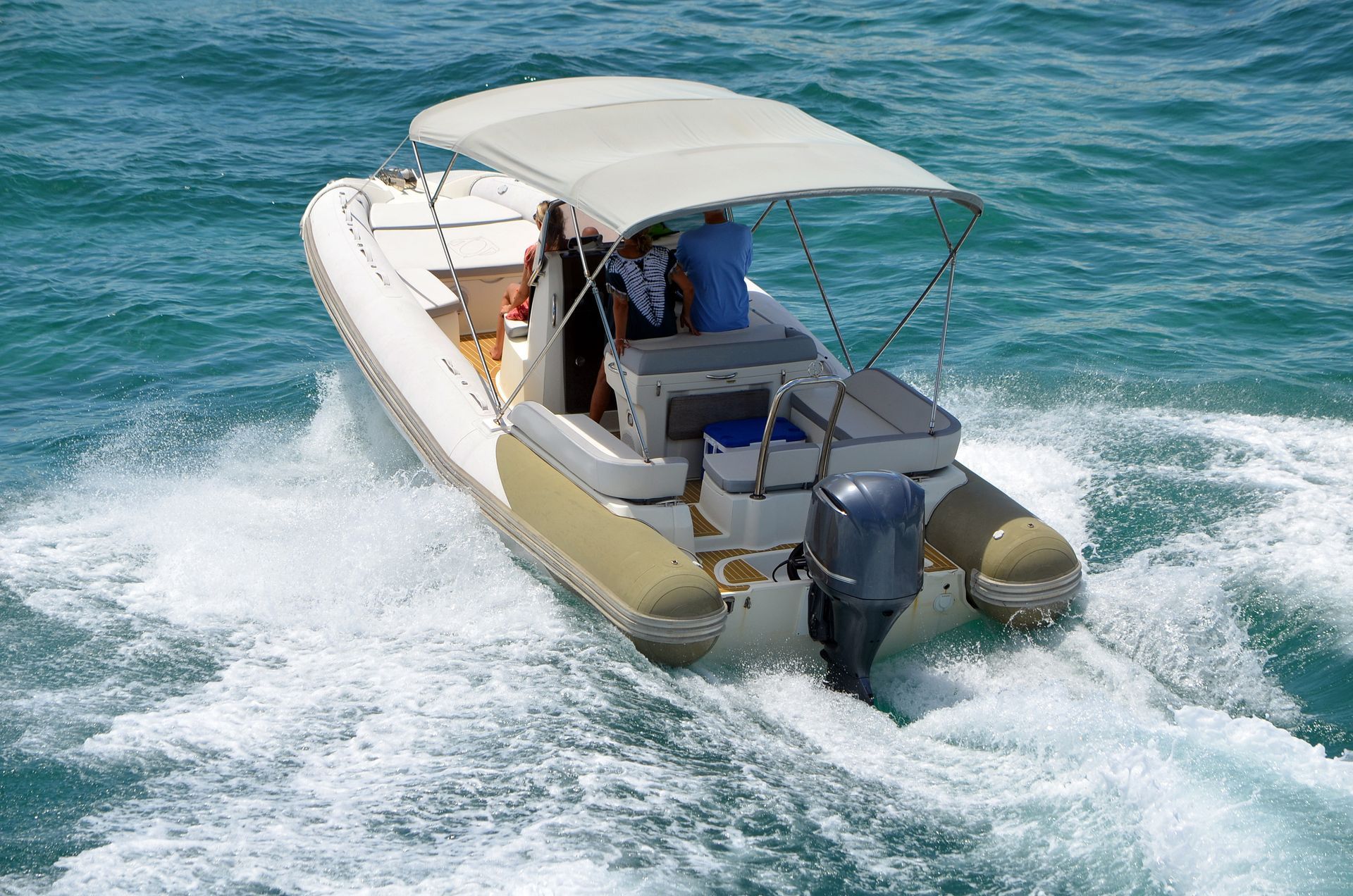 White and beige inflatable boat with motor speeding through teal water; canopy provides shade to people.