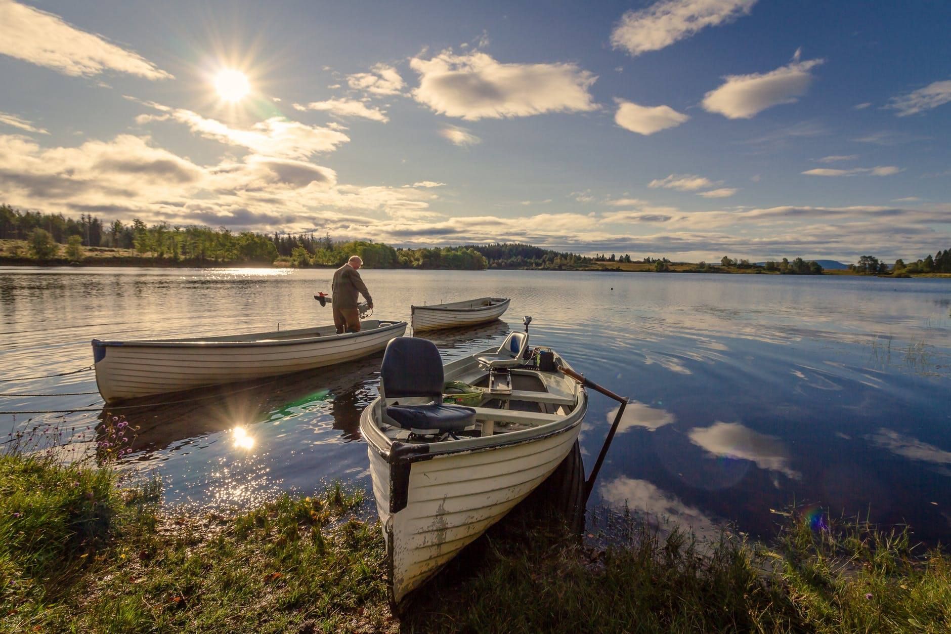 Boats on a calm lake with a person fishing under a bright sun.
