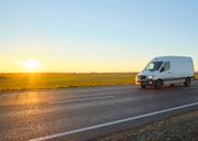 White delivery van driving on a road at sunset, with a field in the background.
