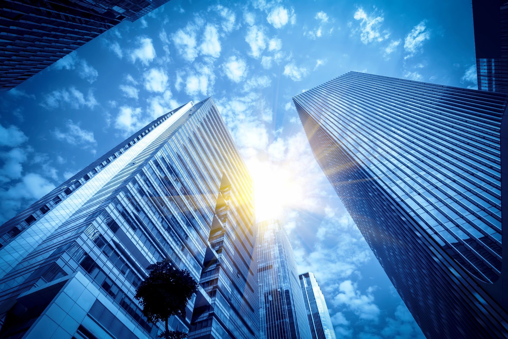 Low-angle shot of tall skyscrapers against a bright blue sky with the sun shining.
