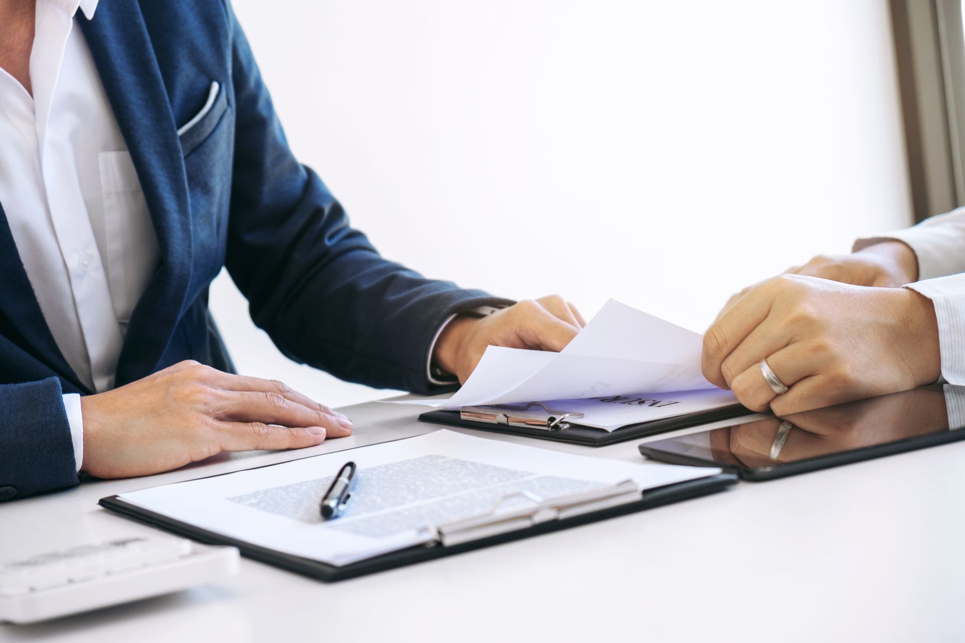 Two people reviewing documents at a table. Hands holding papers, a tablet, and a pen visible.